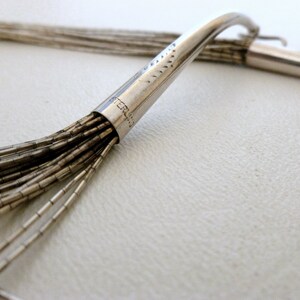 May include: A silver necklace with a clasp that reads "STERLING". The necklace is made of multiple strands of small, silver beads.