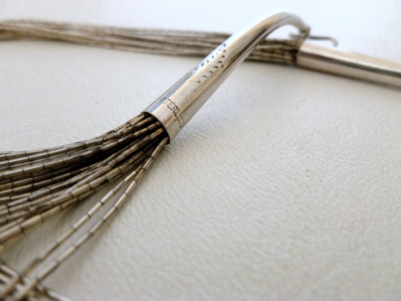 May include: A silver necklace with a clasp that reads "STERLING". The necklace is made of multiple strands of small, silver beads.