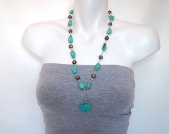 May include: A turquoise and silver necklace with a pendant shaped like an elephant. The necklace features turquoise stones and silver beads. The necklace is displayed on a mannequin wearing a gray tube top.