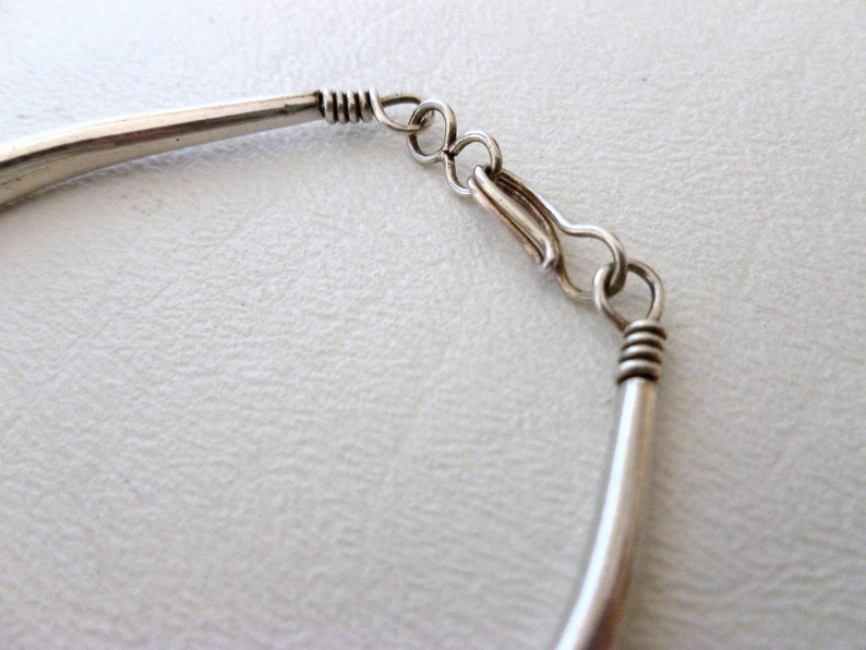 May include: Silver bracelet with a simple, curved design and a lobster claw clasp.