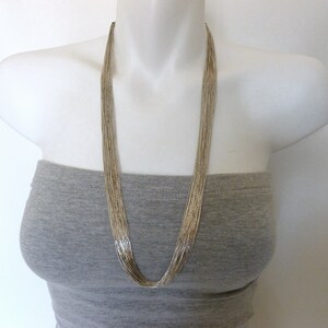 May include: A long silver chain necklace with multiple strands. The necklace is on a white mannequin wearing a gray strapless top.
