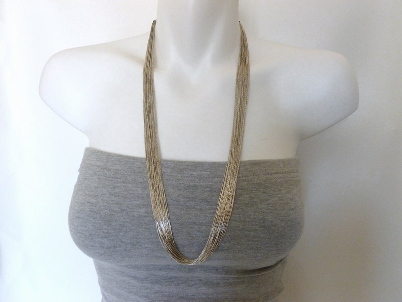 May include: A long silver chain necklace with multiple strands. The necklace is on a white mannequin wearing a gray strapless top.