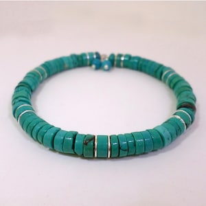 Puede incluir: Pulsera de cuentas turquesas con detalles plateados. La pulsera presenta cuentas turquesas redondas y planas ensartadas con espaciadores plateados. La pulsera es de un color verde azulado vibrante y se muestra sobre un fondo blanco.