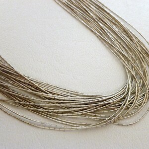 May include: A silver necklace made of many thin, linked chains. The necklace is laid out in a circle on a white surface.