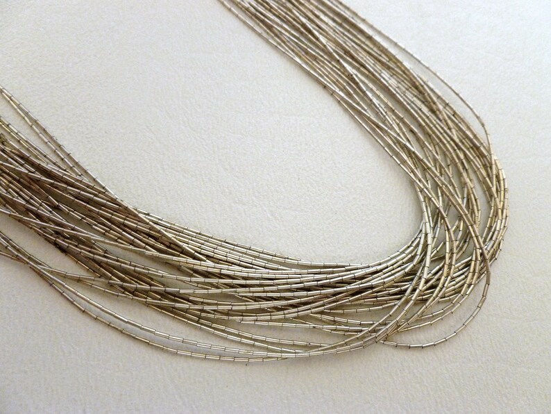 May include: A silver necklace made of many thin, linked chains. The necklace is laid out in a circle on a white surface.