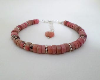 May include: A pink and silver bracelet featuring a series of flat, round, pink beads. Small silver beads separate the pink beads. A small pink heart charm hangs from the bracelet.