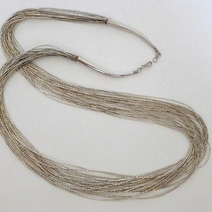 May include: A long silver necklace made of many thin strands of beads. The necklace is approximately 30 inches long and has a simple clasp.