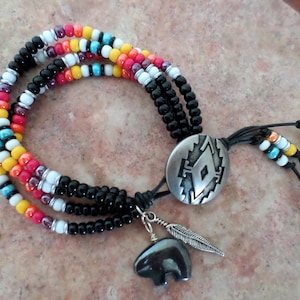May include: A multi-strand beaded bracelet with a Southwestern design. The bracelet features black, white, red, yellow, and turquoise beads. A silver-tone oval pendant with a geometric design and a bear charm with a feather dangle.