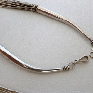 May include: A silver necklace with a chain made of multiple strands of thin silver wire. The necklace has a simple, curved clasp.