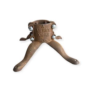Peut inclure: Un support de sapin de Noël vintage en fonte, avec une finition marron vieillie. Le support porte l'inscription "A Merry Xmas" et "Smart Tree Stand No. 1". Il possède une base circulaire avec trois pieds incurvés et des boulons argentés.