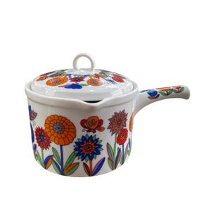 Peut inclure: Casserole en céramique blanche avec couvercle, ornée d'un motif floral vibrant en orange, bleu et rouge. La poignée et le couvercle présentent également le même design coloré. Un charmant article de cuisine.