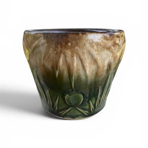 May include: A handcrafted ceramic bowl with a unique design. The bowl features a gradient of colors, transitioning from a dark brown rim to a light tan center, and a deep green base. The exterior has a textured, carved pattern.