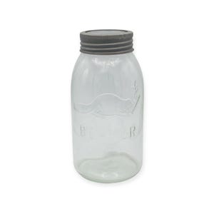 May include: Clear glass jar with a silver metal lid. The jar has a rounded shape and features an embossed design of a beaver and the word "BEAVER". The jar is empty and sits on a white background.
