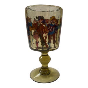 May include: A vintage, olive-green glass goblet with a detailed painted scene of figures in Renaissance-era clothing. The goblet has a rounded bowl, a bulbous stem, and a circular base. The painted figures are in shades of red, blue, and yellow.