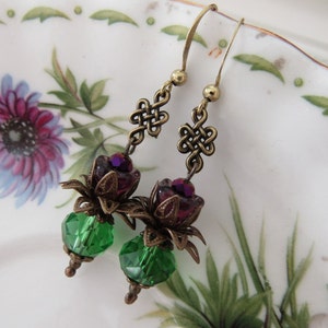 May include: A pair of dangle earrings with green and purple glass beads, bronze filigree, and a knot design.