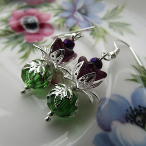 May include: A pair of silver earrings with green and purple glass beads. The earrings feature a delicate floral design.