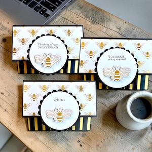 May include: A white ceramic mug with a black handle and the text "But First, Coffee" in a black, bold font. The mug is on a wooden surface. The mug is approximately 10 cm tall.