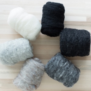 May include: Six balls of wool yarn in various shades of gray, black, and white. The balls are arranged in a circle on a light wood surface.
