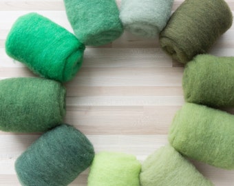 May include: A circle of ten different shades of green wool roving, arranged in a circle on a light wood surface.
