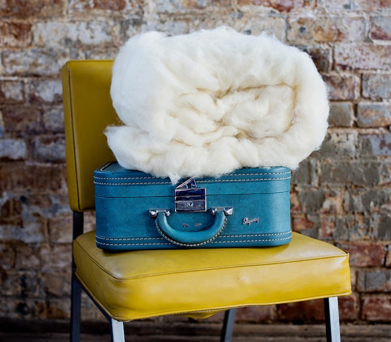 May include: A vintage blue suitcase with a silver lock and the word "Skyway" on the front, sitting on a yellow chair. A large white fluffy ball of wool sits on top of the suitcase.
