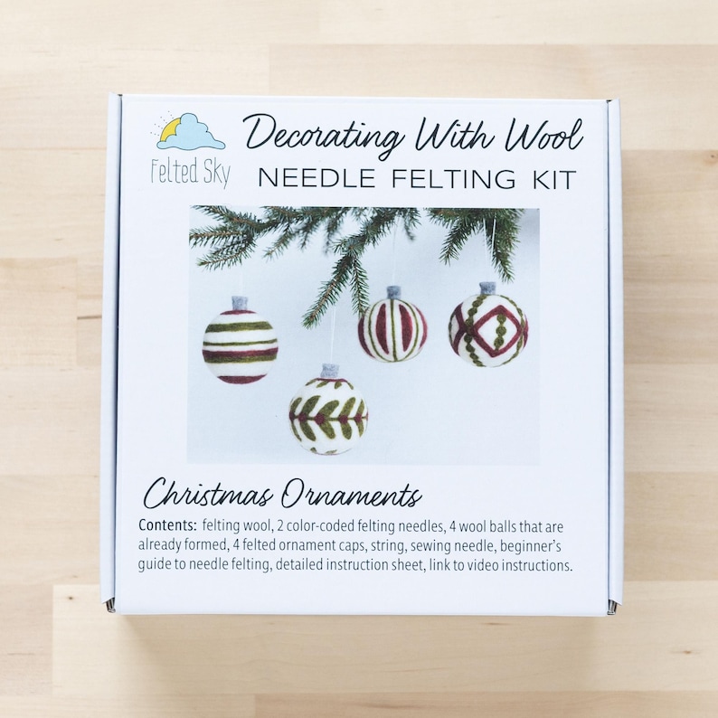 Op de afbeelding: Een witte doos met een naaldviltset om kerstversieringen te maken. De doos heeft een afbeelding van vier vilten ornamenten met verschillende ontwerpen. De tekst op de doos luidt "Decorating With Wool Needle Felting Kit" en "Christmas Ornaments".