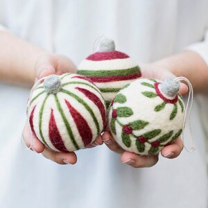 May include: Three handmade felt Christmas ornaments in white, green, and red. The ornaments are decorated with stripes and holly.