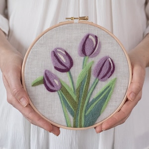 May include: A close-up of a purple and green embroidery hoop with a design of four purple tulips with green leaves.