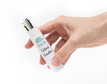 May include: A white tube with a blue and yellow cloud design and the text "Felted Sky Felter's Needles". The tube contains a set of colorful felting needles.