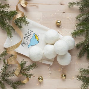 May include: A white cotton bag with the text "Sky Panda" and a blue cloud with a yellow sun graphic. The bag contains six white wool dryer balls.