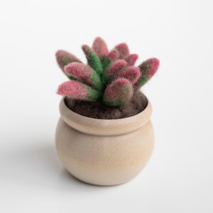 May include: A small potted succulent plant with pink and green felt leaves. The plant is in a light brown wooden pot.