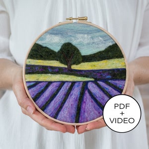 Op de afbeelding: Een naaldgevoelde landschapsscène van een lavendelveld met een boom en een blauwe lucht. De scène is ingelijst in een houten hoepel. De afbeelding bevat de tekst "PDF + VIDEO".