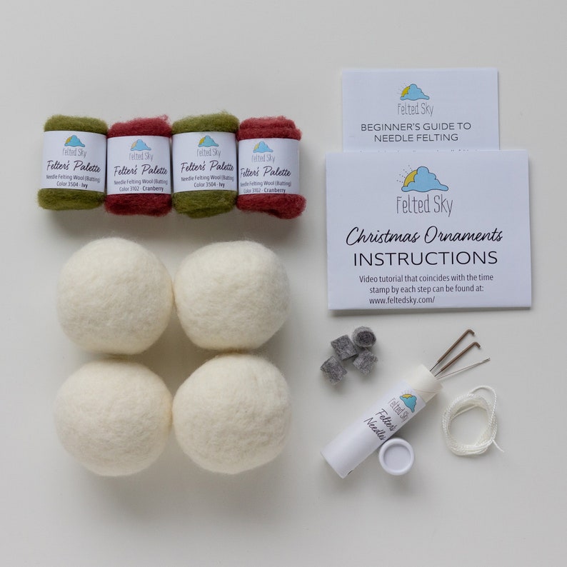 Op de afbeelding: Een naaldvilten set voor het maken van kerstversiering. De set bevat vier ballen witte wol, vier strengen wol in groen, rood en ivoor, een pak naaldvilten naalden, een klein pak grijze vilten wol en instructies. De instructies bevatten een link naar een video tutorial.