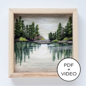 Op de afbeelding: Een ingelijst naaldgevoeld kunstwerk dat een meer scène voorstelt met bomen die in het water worden weerspiegeld. Het kunstwerk is in een licht houten lijst. De tekst "PDF + VIDEO" is zichtbaar in de rechterbenedenhoek van de afbeelding.