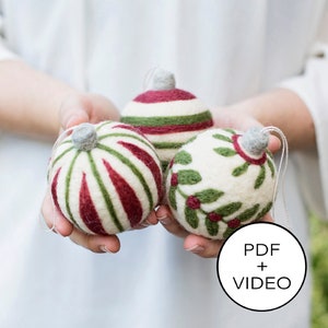 May include: Three felt Christmas ornaments in a person's hands. One ornament is white with green holly leaves and red berries. The other two ornaments are white with red and green stripes.