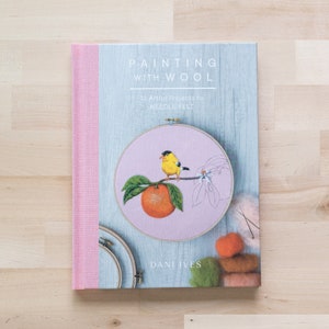 May include: A book titled "Painting with Wool: 16 Artful Projects to Needle Felt" by Dani Ives. The cover features a close-up of a needle felted bird on a branch with an orange, inside a hoop.