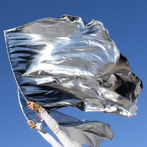 May include: A silver metallic fabric flag being waved in the air against a blue sky.