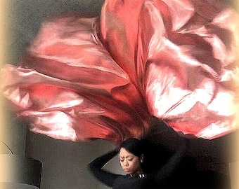 May include: A woman wearing a black shirt is holding a large, flowing, pink fabric over her head. The fabric is draped over her head and shoulders, creating a dramatic effect.