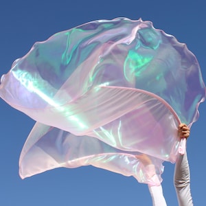 May include: A large, iridescent pink fabric dance prop, also known as a worship flag, is being held by a person's hands against a blue sky background.
