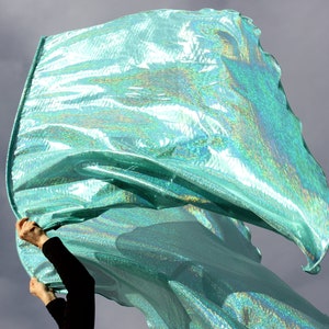 May include: A person holding a large, iridescent teal fabric flag. The fabric is flowing in the wind, creating a dynamic and colorful display.