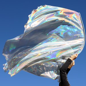 May include: A silver iridescent fabric flag being waved in the air against a blue sky.