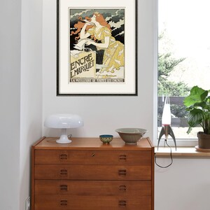 May include: A vintage poster advertising "Encre L'Marquet" ink. The poster features a woman in a yellow dress writing with a pen. The text "La Meilleure de Toutes les Encres" is at the bottom of the poster.