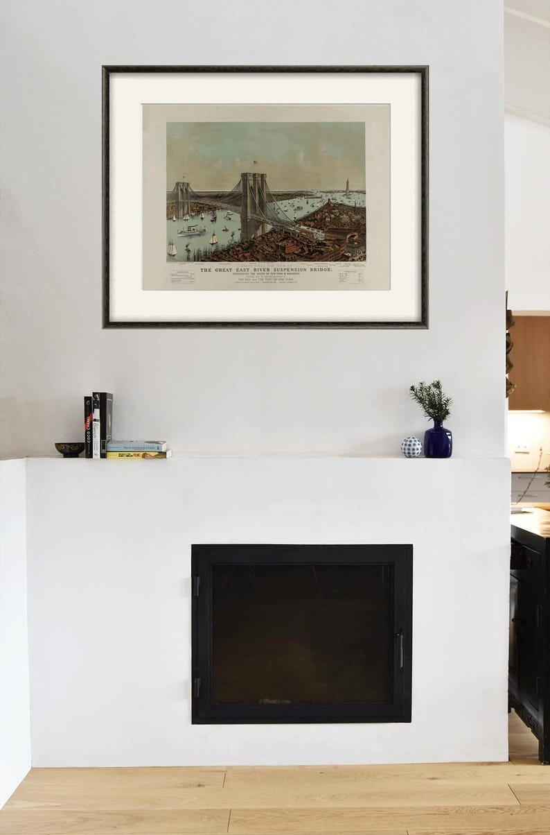 May include: Framed vintage print of the Great East River Suspension Bridge, with boats and buildings. The print is in a black frame, mounted on a white wall above a fireplace. A small blue vase and books are on the mantel.