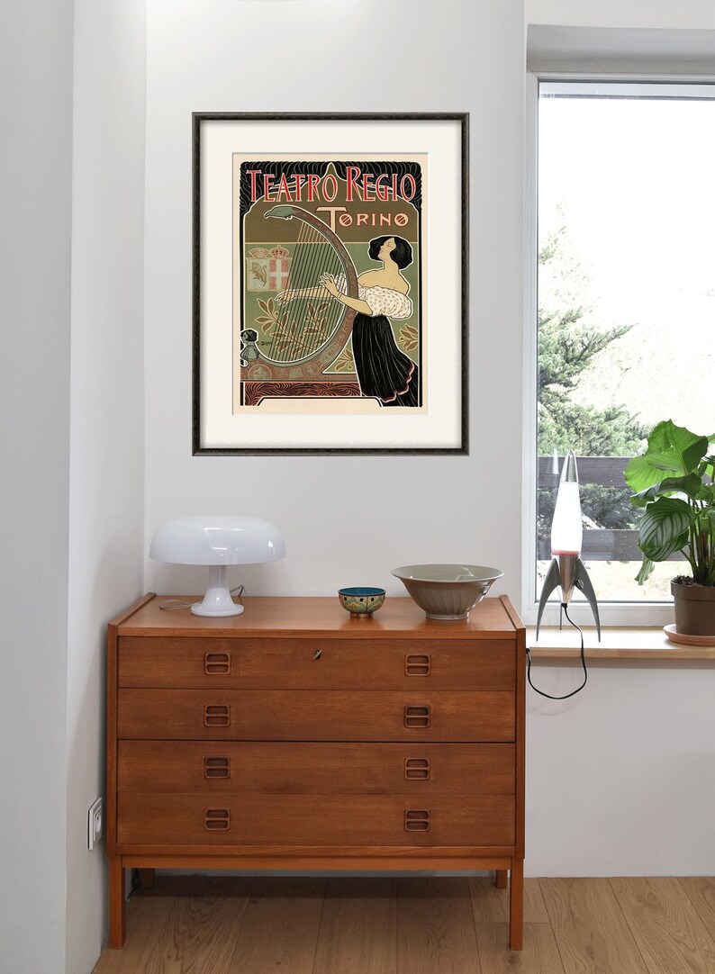Peut inclure: Une affiche vintage pour le Teatro Regio de Turin, en Italie. L'affiche repr&eacute;sente une femme jouant du harpe avec un blason et les mots "Teatro Regio Torino" en arri&egrave;re-plan.