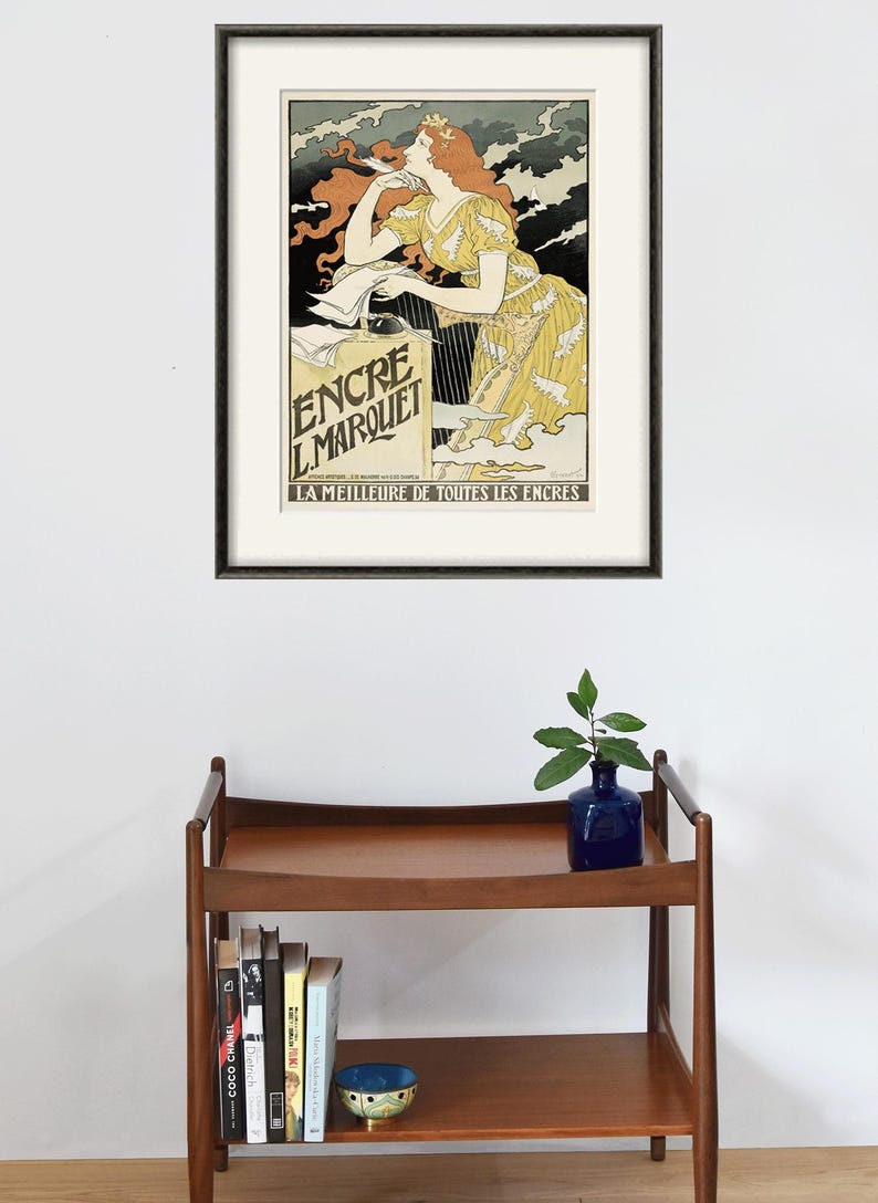 May include: A framed vintage poster advertising "Encre L.Marquet" ink. The poster features a woman with red hair writing with a quill pen. The text on the poster reads "La Meilleure de Toutes les Encres" which translates to "The Best of All Inks".