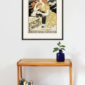 May include: A framed vintage poster advertising "Encre L'Marquet" ink. The poster features a woman in a yellow dress with red hair, holding a pen and looking at a bottle of ink. The text on the poster reads "La Meilleure de Toutes les Encres", which translates to "The Best of All Inks".