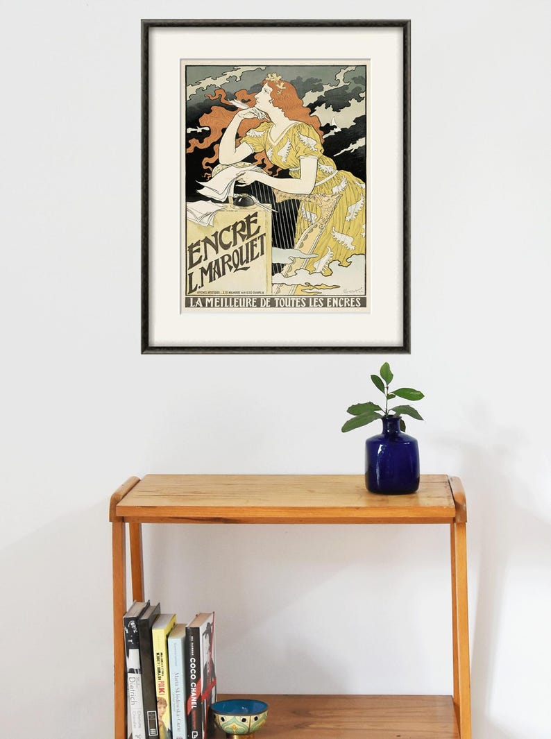 May include: A framed vintage poster advertising "Encre L'Marquet" ink. The poster features a woman in a yellow dress with red hair, holding a pen and looking at a bottle of ink. The text on the poster reads "La Meilleure de Toutes les Encres", which translates to "The Best of All Inks".