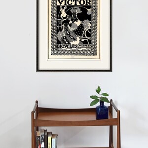 Pu&ograve; includere: Un poster vintage in bianco e nero che pubblicizza Victor Bicycles Overman Wheel Company. Il poster presenta una donna che guida una bicicletta con un design floreale decorativo.
