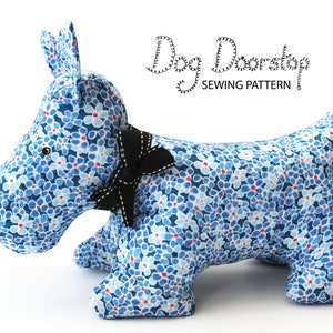 May include: A blue and white floral dog doorstop with a black bow. The doorstop is shaped like a Scottish Terrier and says "Dog Doorstop Sewing Pattern" on the top.
