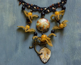 May include: Handmade beaded necklace featuring a central pendant with an orange and gold design. The necklace includes black, brown, and yellow beads, with additional decorative elements. The necklace has a tribal or bohemian aesthetic.