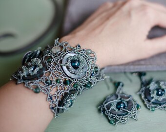 May include: A silver and blue beaded bracelet with a floral design and a large, round, blue gemstone in the centre. The bracelet is paired with matching earrings with a similar design.